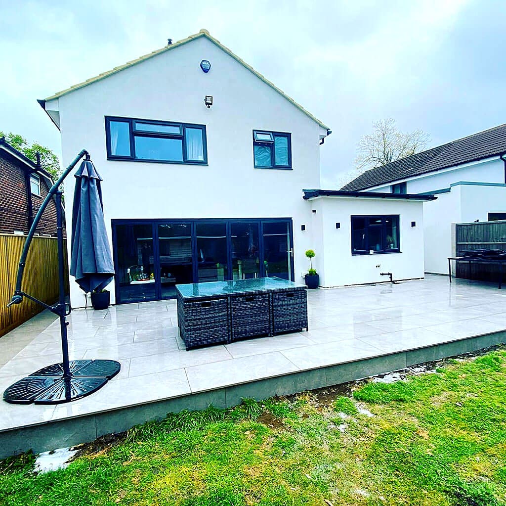 White rendered rear extension with wide bifold doors and a paved terrace, built by Bell & Collier Construction